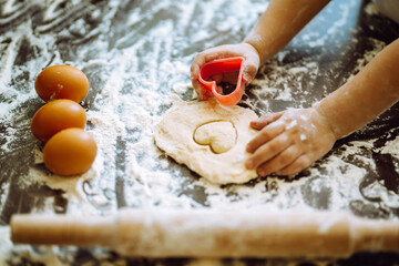 A little child  cutting out shapes heart dough. Easter baking preparation. Children's art project, a craft for children.