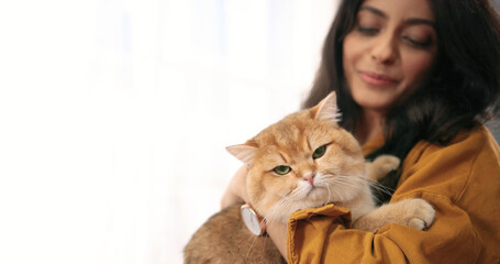 Side view of Hindu beautiful young woman holding in hands fluffy cute big cat in room near window and speaking with pet. Relaxed cute animal pet in owner's arms, pet lover. Close up concept