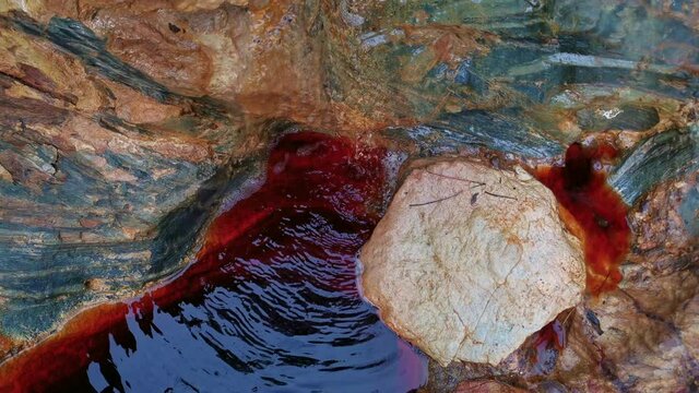 Reddish running water between rocks near the source of the Rio Tinto in Andalusia