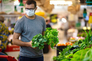 Alarmed male wears medical mask against coronavirus while grocery shopping in supermarket or store- health, safety and pandemic concept - young man stockpiling food in fear of covid-19