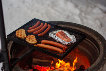 Salmon, sausages and bread on the grill over the fire.