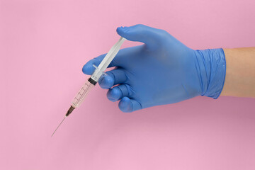 Doctor's hand holding syringe in blue gloves on pink background.