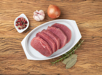 Cut raw eye round meat over white plate with seasonings