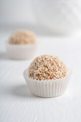 Organic vegetarian sweet truffles dessert or homemade nut vegan energy balls made of sesame, hazelnut and dates fruit on white wooden background at kitchen ready to eat. Vertical image