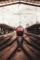Vertical symmetrical view of a railroad station depot with a triangle roof, a modern red train locomotive being on maintenance in between two covered platforms, a railway arrow in the foreground