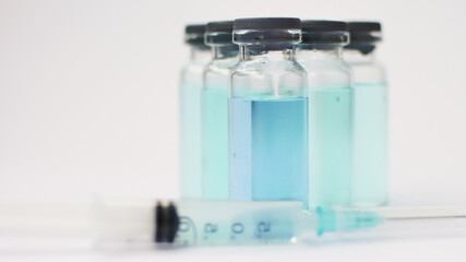 Vial vaccine, glass ampoules with transparent and blue liquid, a syringe is lying near on white background, global vaccination concept