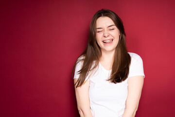 Cheerful happy girl with long hair in a white T-shirt in braces closing her eyes laughs opening her...