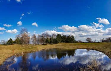 Sunny spring landscape with small lakes on flooded meadows on the banks of Kisezers in Riga, Latvia.White cumulus clouds are reflected in the water.