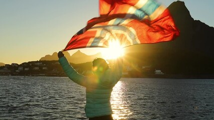 Woman waving the flag of Norway at sunset