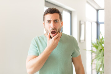 handsome man with mouth and eyes wide open and hand on chin, feeling unpleasantly shocked, saying...