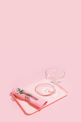 Romantic vertical composition with empty wine glass, napkin, spoon and flower on plastic tray on a pink tray on a rose background with copy space. Table setting for one person. Home relax concept