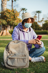 Fototapeta premium Student wearing a hat and a medical mask using a mobile phone in the park.