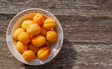 Ripe apricots in a rustic plate on the table, on wooden background.