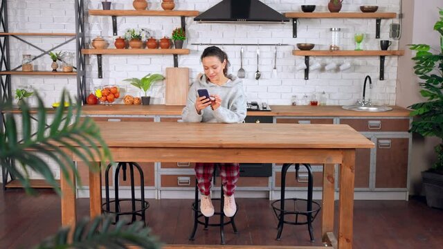 young woman using smartphone looking photos in social media slow motion morning at home with device kitchen interior