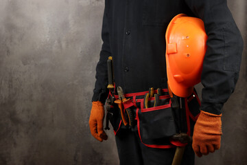 construction worker in a belt with tools and a helmet in hand