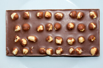 close-up of milk chocolate bar with whole hazelnuts on white background. selective focus. top view