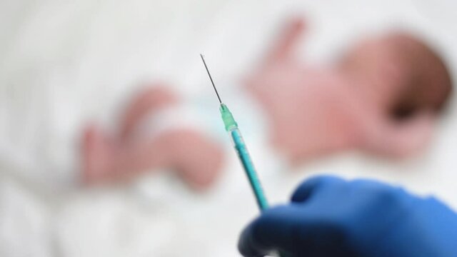 Pediatrician vaccinating newborn baby. Vaccine, Vaccination for infant child Softfocus Syringe in hands of a nurse  and blurred background of infant  baby on white. Doctor in blue gloves close up.