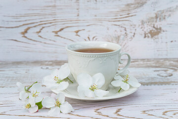 Spring tea time concept. White cup of tea or coffee in retro style and apple blossom on white paint wooden background. Space for text