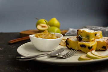 Sliced pie on a white plate with pear jam on a black table. Green pears in the background are blurred. Morning breakfast