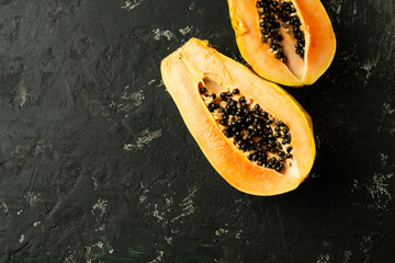 Sliced fresh and tasty papaya on a black textured background. Tropical fruit. Copy space