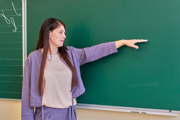 The young teacher points to the blackboard with her hand, copy space.