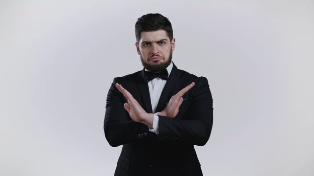 Portrait of serious man in tuxedo disapproving with no crossing hands sign make basta, negation, enough gesture. Denying, Rejecting, Disagree. Portrait of handsome guy on white background