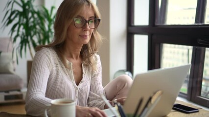 Woman using laptop for self education and sitting at table in apartment room. - Powered by Adobe