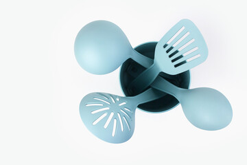 Fototapeta premium Blue plastic kitchen tools for cooking on a white background. Spatulas and ladles in a plastic container.