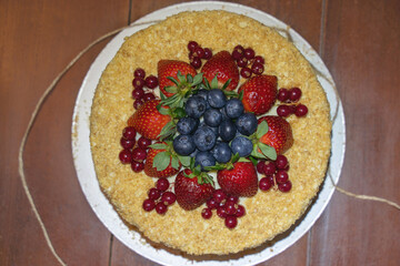 Top view of cake decorated with mixed berries, settled on wooden table. Blueberries, strawberries and redcurrant. Soft selective focus, copy space.