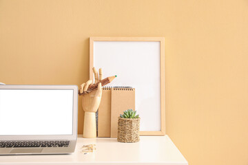 Wooden hand with laptop and pencil on table near color wall in room