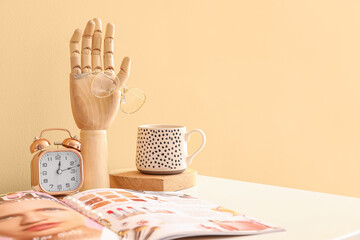 Wooden hand with fashion magazine and female jewelry on table in interior of room