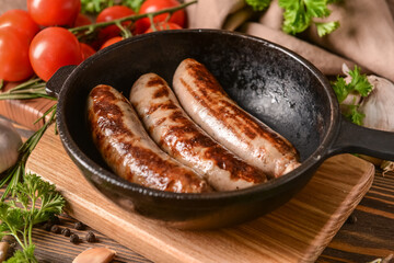 Frying pan with delicious grilled sausages on wooden background
