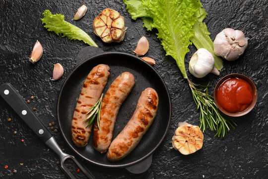 Frying pan with delicious grilled sausages on dark background