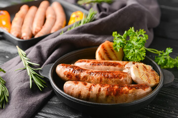 Frying pans with delicious grilled sausages on dark wooden background