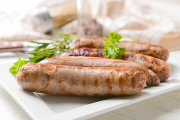 Plate with delicious grilled sausages on light background