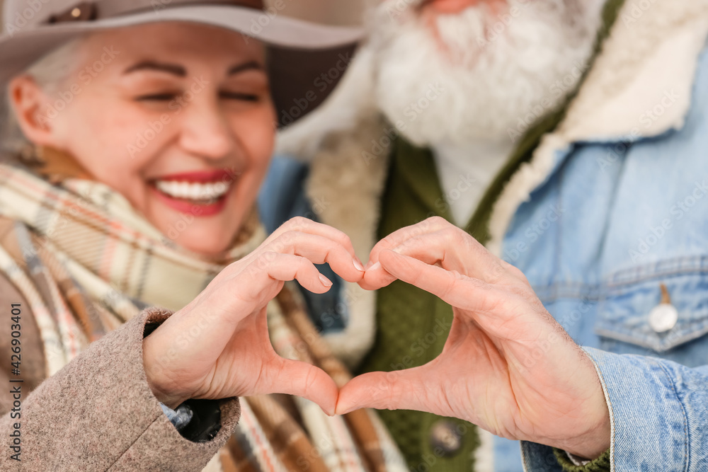 Wall mural happy mature couple making heart with their hands outdoors on winter day