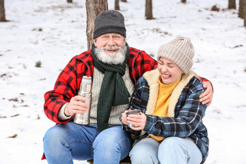 Fototapeta na wymiar Happy mature couple drinking hot tea in forest on winter day