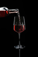 Pouring of wine from bottle into glass on dark background