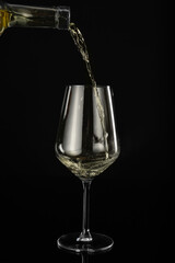 Pouring of wine from bottle into glass on dark background