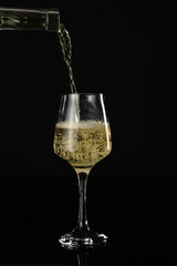 Pouring of wine from bottle into glass on dark background