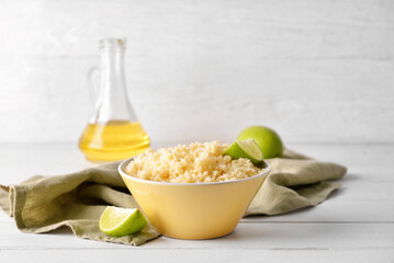Bowl with tasty couscous and lime on light wooden background