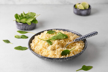 Bowl with tasty couscous and spinach on light background