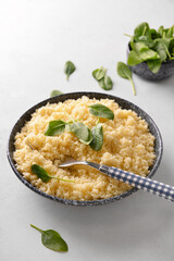 Bowl with tasty couscous and spinach on light background