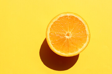 Half of orange on yellow background. Citrus fruit slice on colored backdrop. Top view, copy space....
