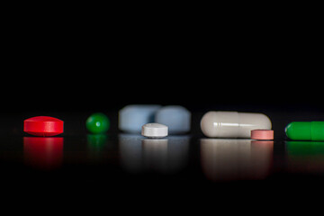 medicamentos en forma de pastillas de distintos colores reflejándose sobre una plataforma negra 