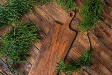 Cutting board on a wooden table background surrounded by pine branches, top view. 