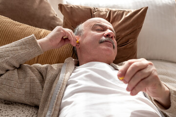 Obraz na płótnie Canvas Senior stressed man holding a yellow earplug trying to sleep having insomnia