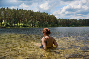 Dziewczyna wypoczywająca nad czystym jeziorem w promieniach letniego słońca, w tle zielony las.