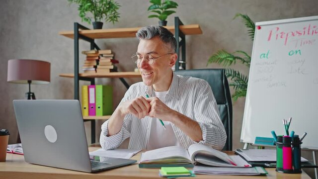 Happy remote work. Cheerful mature teacher video chatting with students online via laptop, laughing and joking