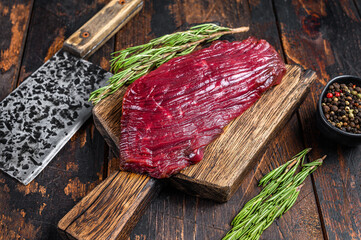 Venison raw meat steak on a cuuting board with rosemary. Black background. Top view